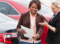 Woman looks at paper and listens to salesperson at a car dealership