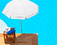 Sun umbrella next to swimming pool with hat and towel on a table.