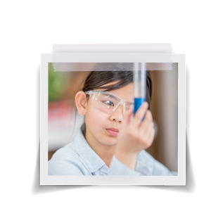 Girl wearing safety glasses examining blue liquid in a test tube.