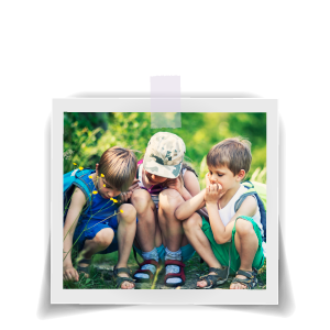 Three boys sitting in grassy area looking thoughtfully at something on the ground.