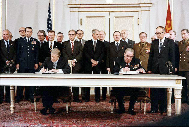 President Carter and Soviet General Secretary Brezhnev signing the SALT II treaty, with a group of men standing witness behind them