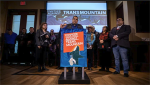 protestors at podium with sign reading "together against Trans Mountain"